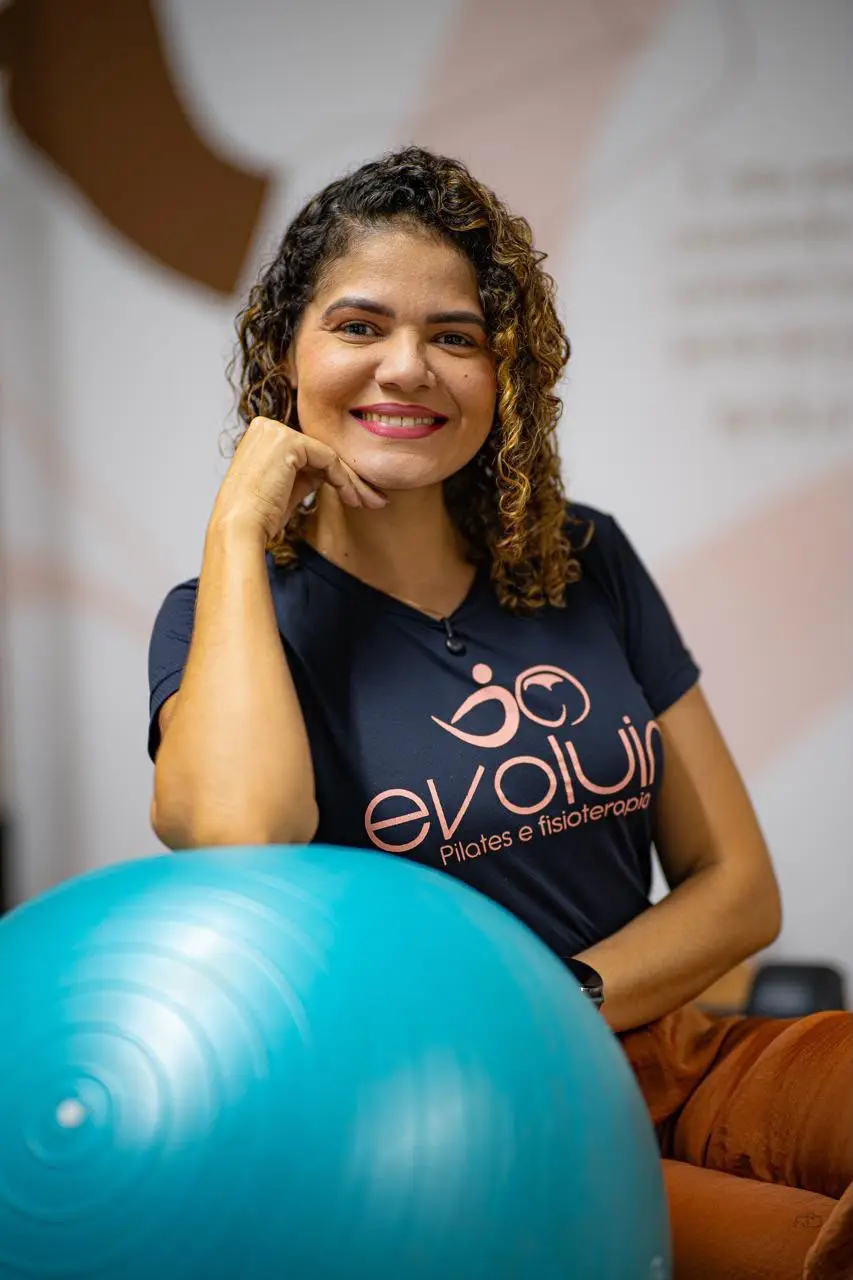 Jennefen Rayka Simões sorrindo no estúdio da Evoluir, com uma bola de Pilates à frente.